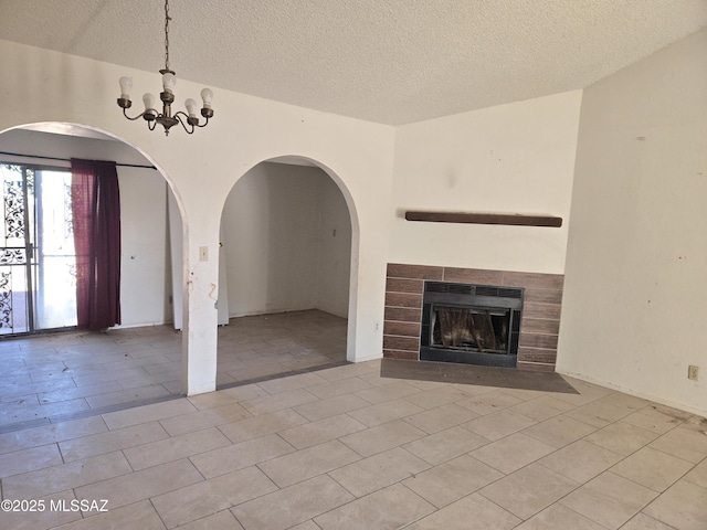 unfurnished living room featuring a textured ceiling, a notable chandelier, and a tile fireplace