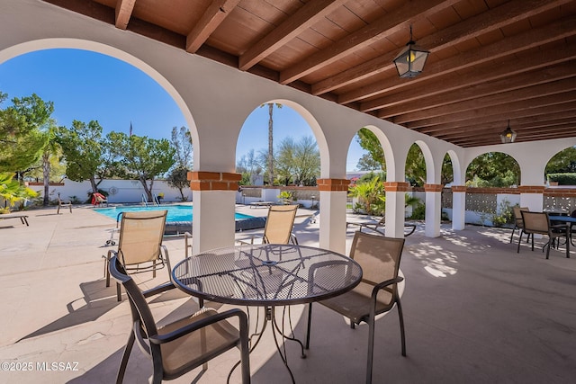 view of patio with a community pool, outdoor dining area, and fence