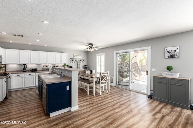 kitchen featuring wood finished floors, visible vents, a sink, white cabinets, and stainless steel gas range oven