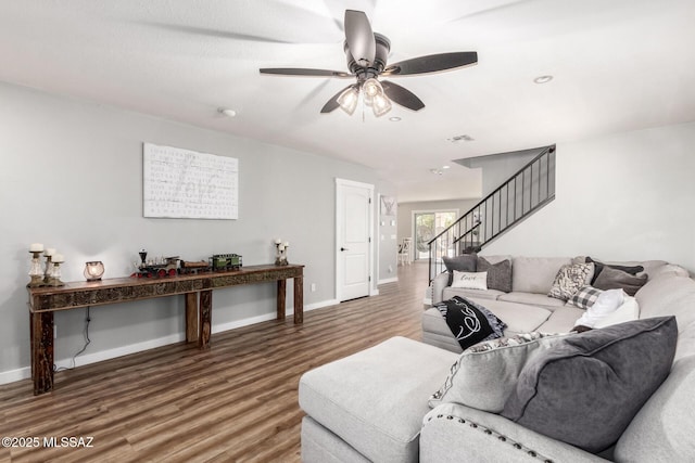 living area with wood finished floors, visible vents, baseboards, ceiling fan, and stairs