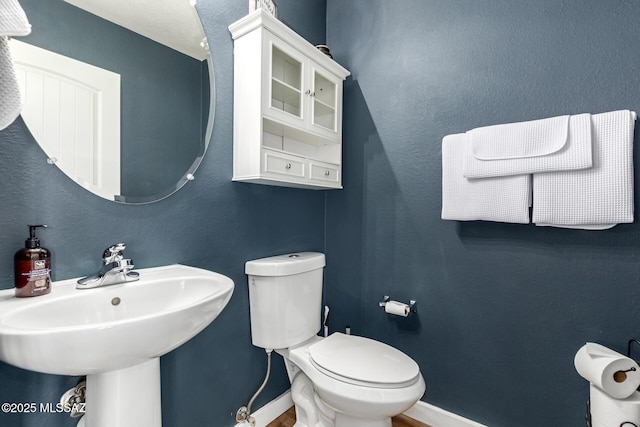 half bathroom with toilet, baseboards, and a sink