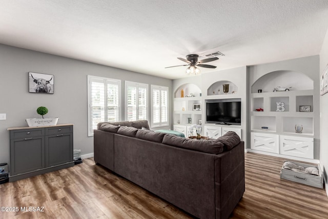 living area featuring visible vents, built in shelves, a textured ceiling, and wood finished floors