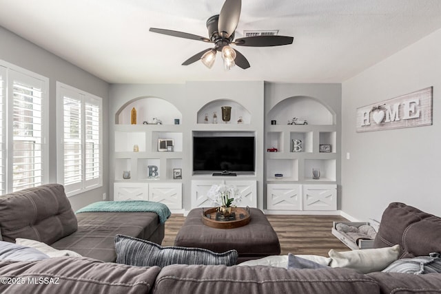 living room featuring visible vents, built in shelves, baseboards, wood finished floors, and a ceiling fan