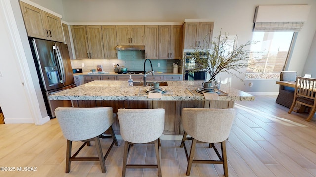 kitchen featuring a kitchen breakfast bar, stainless steel fridge with ice dispenser, tasteful backsplash, and under cabinet range hood