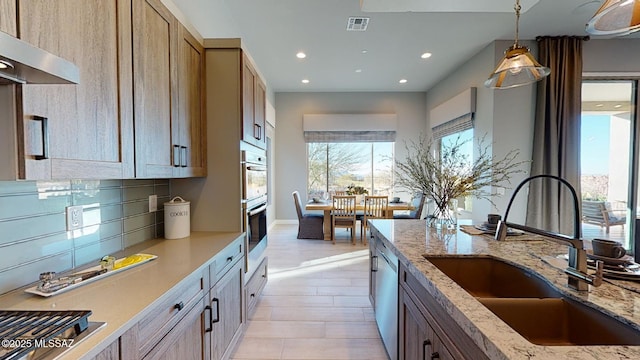 kitchen with visible vents, backsplash, ventilation hood, pendant lighting, and a sink