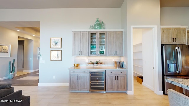 bar featuring baseboards, beverage cooler, decorative backsplash, stainless steel refrigerator with ice dispenser, and a bar