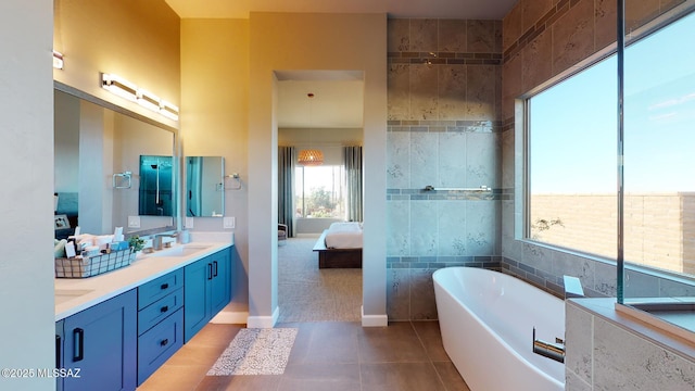 ensuite bathroom with connected bathroom, a freestanding bath, double vanity, tile patterned floors, and a sink