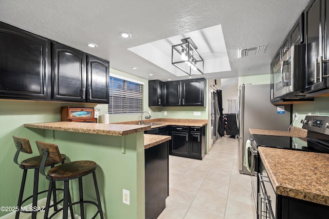 kitchen featuring visible vents, a breakfast bar, dark cabinetry, electric stove, and a sink