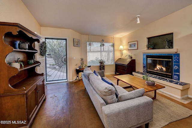 living area with a tiled fireplace, concrete flooring, baseboards, and vaulted ceiling