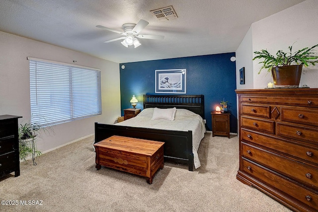 bedroom with visible vents, light carpet, a textured ceiling, baseboards, and ceiling fan