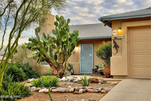 property entrance with stucco siding, an attached garage, and a shingled roof