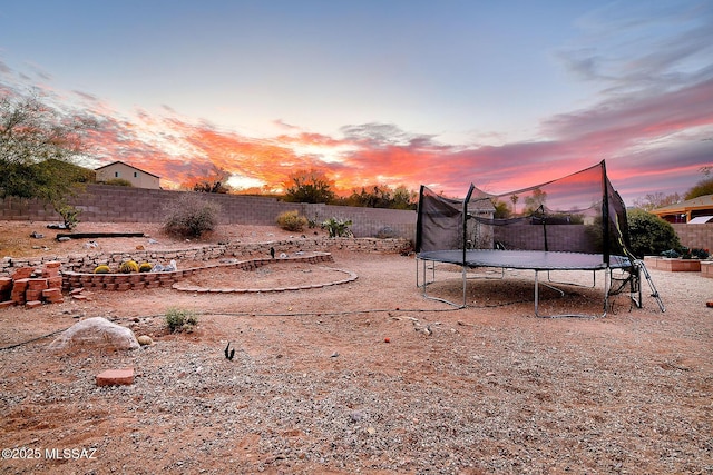 yard at dusk featuring a trampoline and a fenced backyard