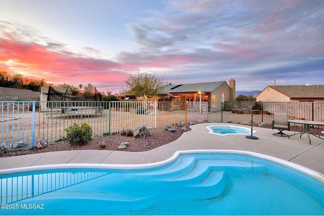 pool at dusk with a patio, a fenced in pool, fence, an in ground hot tub, and a trampoline