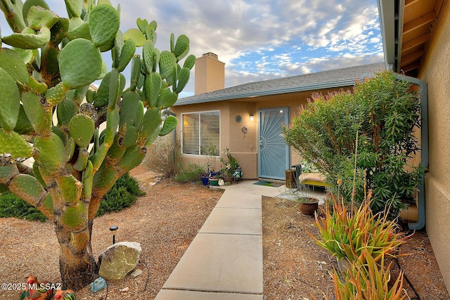 doorway to property featuring stucco siding, a chimney, and roof with shingles