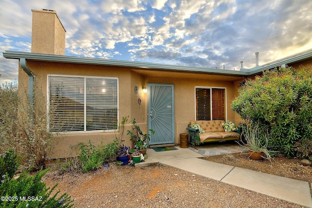 entrance to property with a chimney and stucco siding