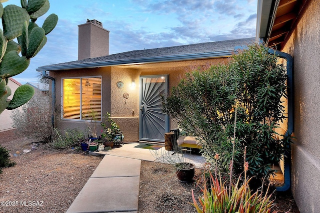 property entrance featuring a patio, a chimney, roof with shingles, and stucco siding