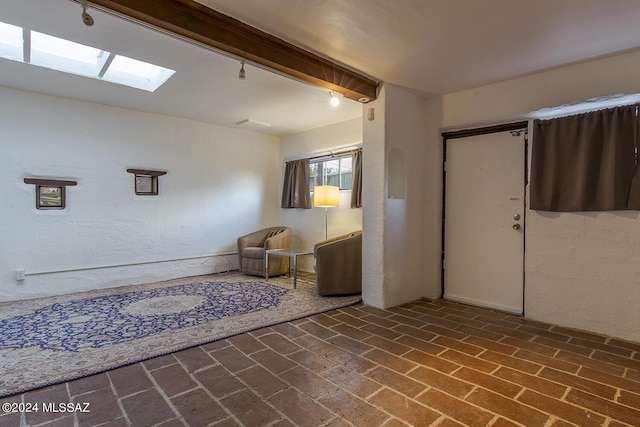 entrance foyer with beamed ceiling, a skylight, brick floor, and a textured wall