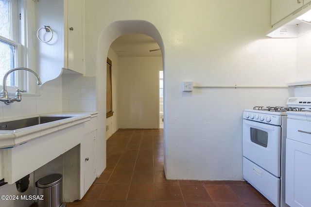 kitchen with arched walkways, white range with gas cooktop, white cabinets, and a sink