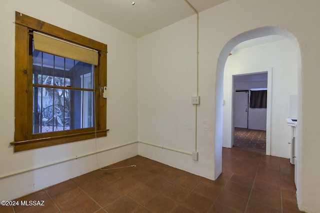 empty room featuring arched walkways and dark tile patterned floors