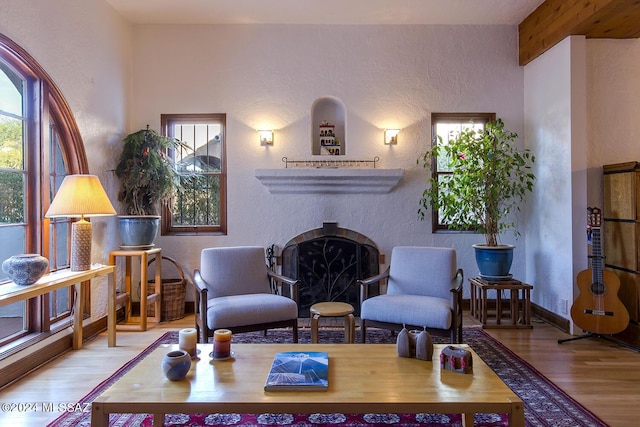 living area featuring beam ceiling, a fireplace, a textured wall, and wood finished floors