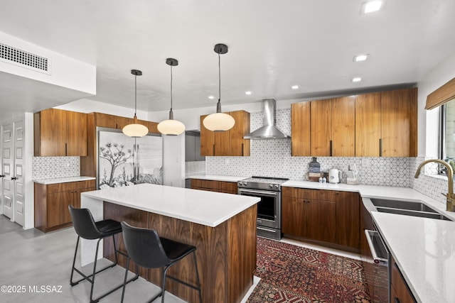 kitchen featuring visible vents, a breakfast bar, a sink, stainless steel appliances, and wall chimney range hood