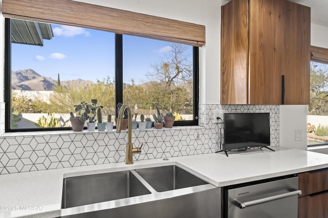 kitchen featuring a sink, dishwasher, brown cabinetry, and light countertops