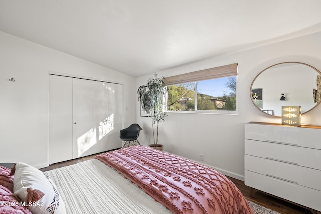 bedroom with a closet, baseboards, dark wood-style flooring, and vaulted ceiling