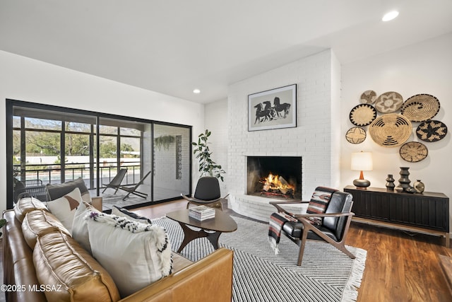 living room with recessed lighting, a brick fireplace, and dark wood-style flooring