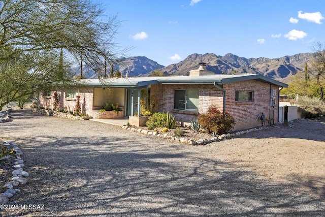 mid-century modern home featuring a mountain view, driveway, brick siding, and a chimney