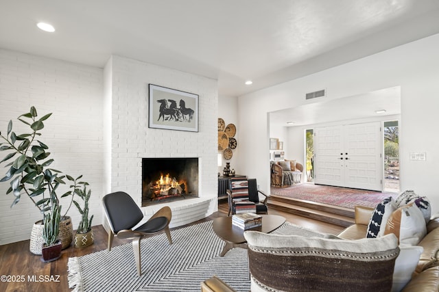 living room with wood finished floors, visible vents, brick wall, a fireplace, and recessed lighting