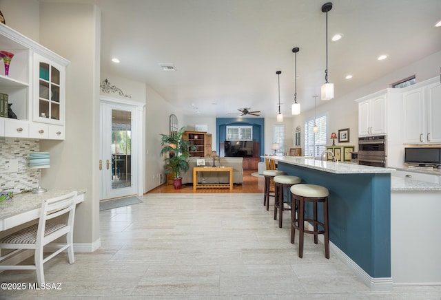 kitchen with a ceiling fan, visible vents, white cabinetry, decorative backsplash, and a kitchen bar