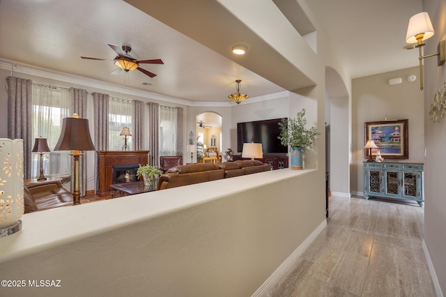 living room with baseboards, ornamental molding, wood finished floors, arched walkways, and a ceiling fan