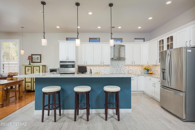 kitchen featuring a breakfast bar area, wall chimney range hood, stainless steel fridge with ice dispenser, and white cabinets