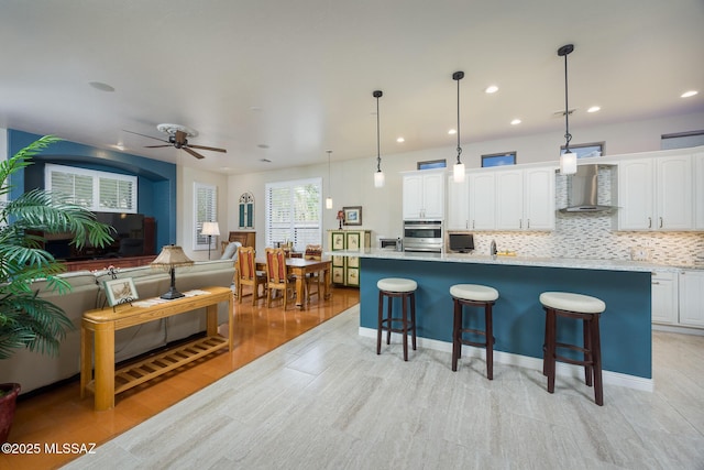 kitchen featuring a kitchen island, a breakfast bar, white cabinets, wall chimney exhaust hood, and a ceiling fan