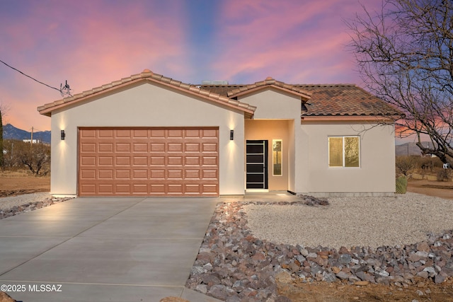 mediterranean / spanish house with stucco siding, driveway, an attached garage, and a tiled roof