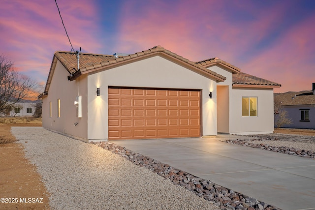 mediterranean / spanish-style home with a tiled roof, a garage, concrete driveway, and stucco siding