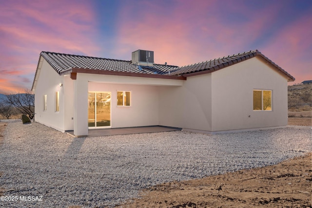 back of property at dusk with a tiled roof, a patio area, central AC, and stucco siding