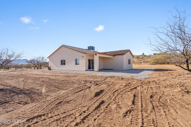 rear view of house with a tile roof, cooling unit, and stucco siding