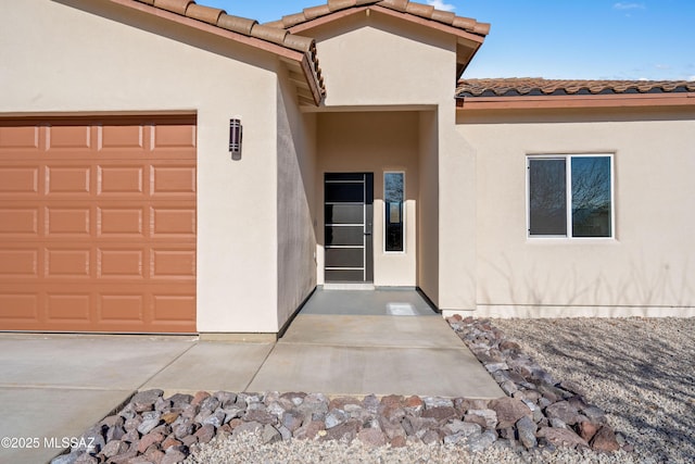 entrance to property featuring stucco siding, an attached garage, and a tiled roof