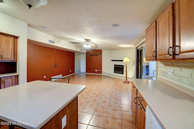 kitchen with visible vents, a ceiling fan, brown cabinetry, and a brick fireplace