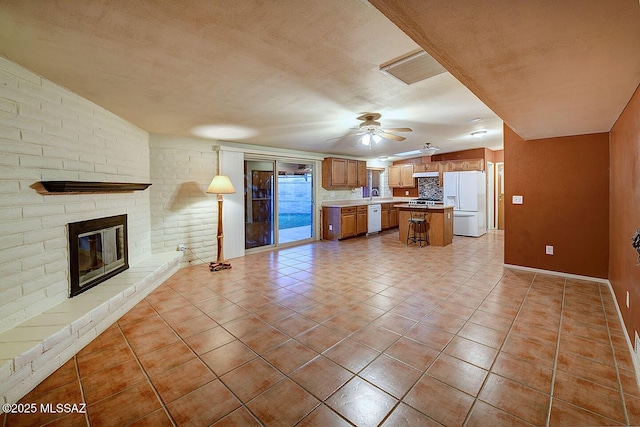 unfurnished living room with a sink, a brick fireplace, light tile patterned flooring, baseboards, and a ceiling fan