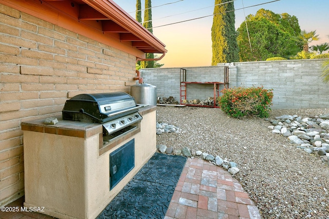 patio terrace at dusk with a fenced backyard, exterior kitchen, and grilling area