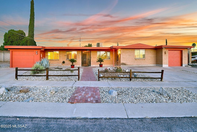 ranch-style house with brick siding, an attached garage, driveway, and a fenced front yard