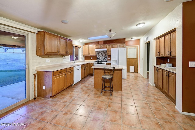 kitchen featuring white appliances, light countertops, a center island, light tile patterned floors, and a skylight