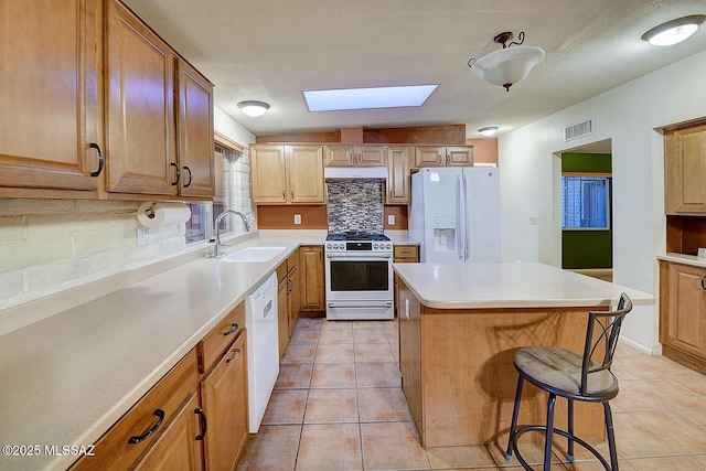 kitchen featuring visible vents, white appliances, tasteful backsplash, a sink, and a skylight