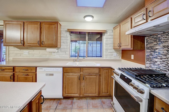 kitchen with decorative backsplash, white appliances, light countertops, under cabinet range hood, and a sink