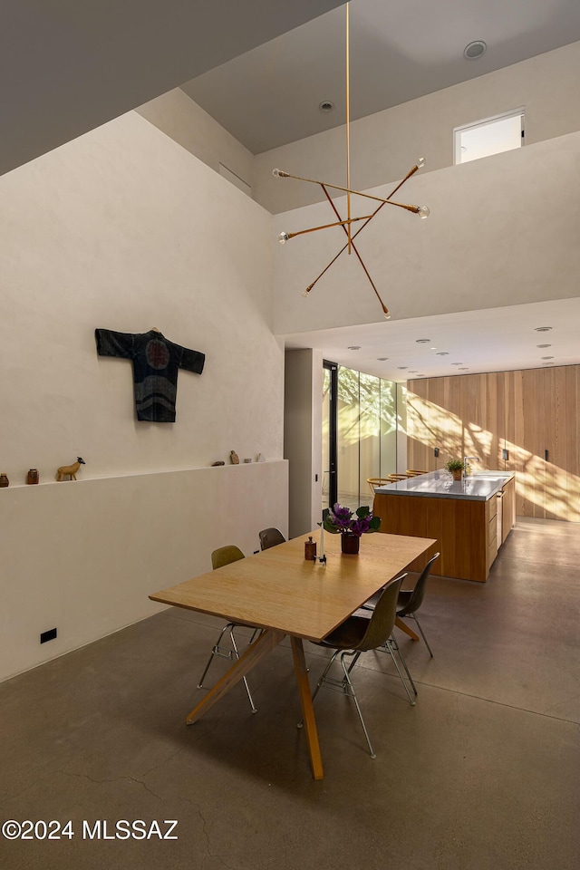 unfurnished dining area featuring a chandelier, finished concrete flooring, and a high ceiling