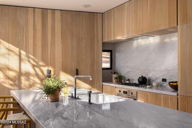 kitchen featuring modern cabinets, wall oven, stainless steel gas stovetop, decorative backsplash, and light stone countertops