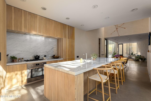 kitchen with finished concrete flooring, a sink, oven, a kitchen bar, and tasteful backsplash