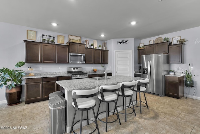 kitchen featuring a sink, dark brown cabinetry, appliances with stainless steel finishes, and a center island with sink